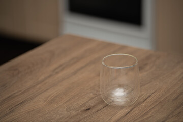 A transparent cup or glass stands on a wooden table in a cozy kitchen