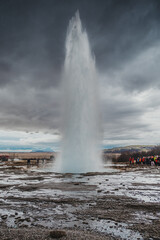 Strokkur geysir erupts under dramatic skies in south Iceland, attracting visitors