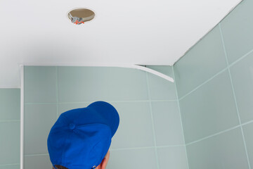A worker in a blue uniform fixes the shortcomings of the installation of a suspended ceiling