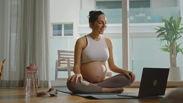 Pregnant woman practicing yoga or Pilates at home, following a lesson on her computer, relaxing and finding balance as she embraces self-care and mindfulness during pregnancy