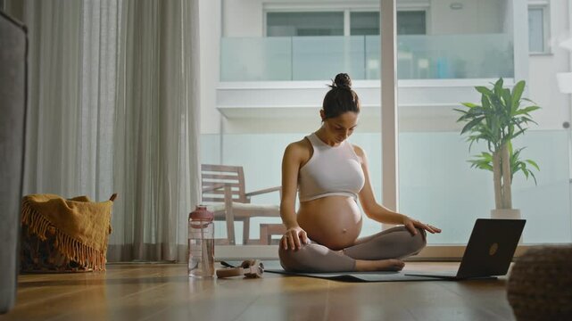 Pregnant woman practicing yoga or Pilates at home, following a lesson on her computer, relaxing and finding balance as she embraces self-care and mindfulness during pregnancy