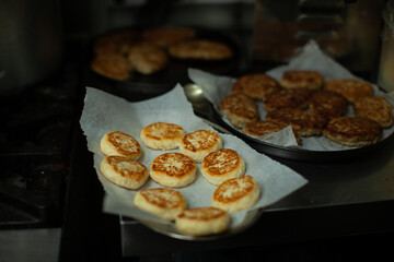 Delicious golden brown syrniki cooling on baking paper after being cooked, with other food items in the background in a professional kitchen setting