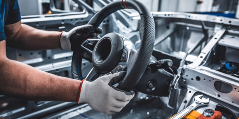 Steering Wheel Installation in Car Factory. Close-up shot of a worker's gloved hands carefully installing a modern steering wheel into the chassis of a car on an assembly line in a factory.