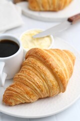 Tasty fresh croissant served with butter and cup of coffee on white table, closeup