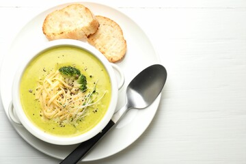 Delicious broccoli cream soup served on white wooden table, flat lay. Space for text