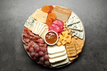 Different types of cut cheese and other snacks on grey textured table, top view