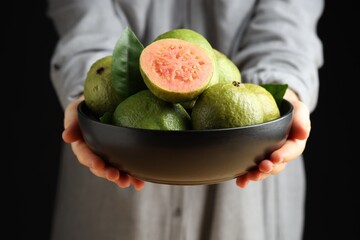 Woman with bowl of fresh guava fruits on black background, closeup