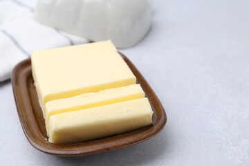 Cut tasty butter in dish on light grey table, closeup. Space for text