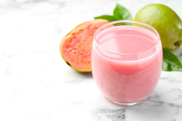 Tasty guava juice in glass, leaves and fruits on white marble table, closeup. Space for text