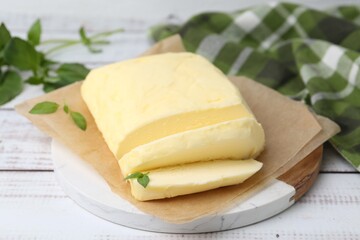 Cut brick of butter and basil on white wooden table, closeup