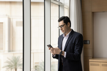 Fototapeta premium Young Arabian businessman holding smartphone, checking messages, scheduling business meetings, browsing wireless internet, lead correspondence to company client by e-mailing, manage workflow using app