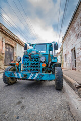 weathered blue tractor parked on a narrow street