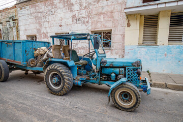 An old blue tractor with a trailer parked on a street in Cuba.
