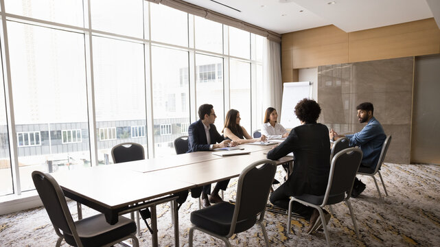 Group of diverse business partners negotiating in modern spacious meeting room, share thoughts and solutions, explain vision or ideas for new corporate project, engaged in briefing event in boardroom