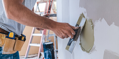 Wall Repair in Progress. A close-up shot of a construction worker's hands skillfully applying joint compound to a wall with a putty knife.
