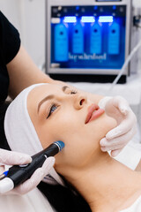 In a cosmetology clinic, a professional female cosmetologist performs a hydrafacial treatment on an...