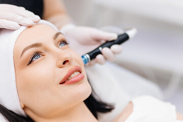 In a cosmetology clinic, a professional female cosmetologist performs a hydrafacial treatment on an attractive woman. Concept of beauty, skincare, and rejuvenation with advanced facial procedures.