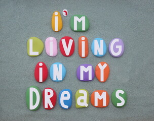 I am living in my dream, creative slogan composed with multi colored hand painted stone letters over green sand