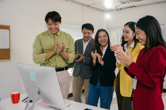 Diverse group of smiling business professionals is applauding a successful online presentation or video conference in a bright modern office, showing teamwork and achievement