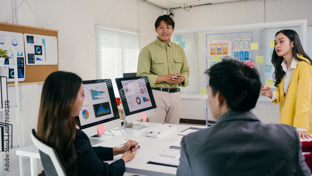 Poster Asian businesspeople are discussing a project together during a business meeting, analyzing graphs and charts displayed on a computer and a whiteboard with sticky notes