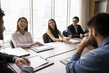 Group of happy diverse teammates, corporate staff members laughing during briefing event gathered at conference table to share creative solutions, strategy, joint task or project planning. Business