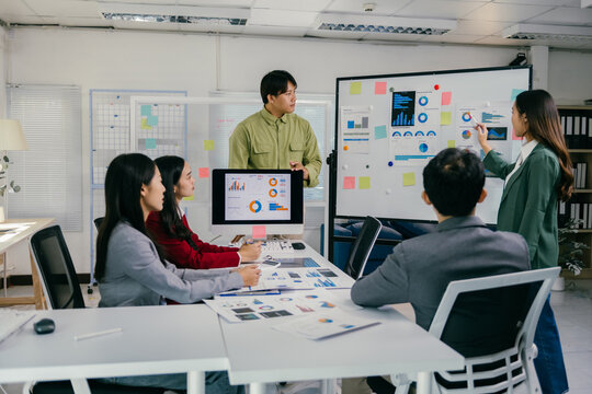 Group of young asian businesspeople discussing charts and graphs on an interactive whiteboard during a presentation meeting focused on company growth and financial analysis