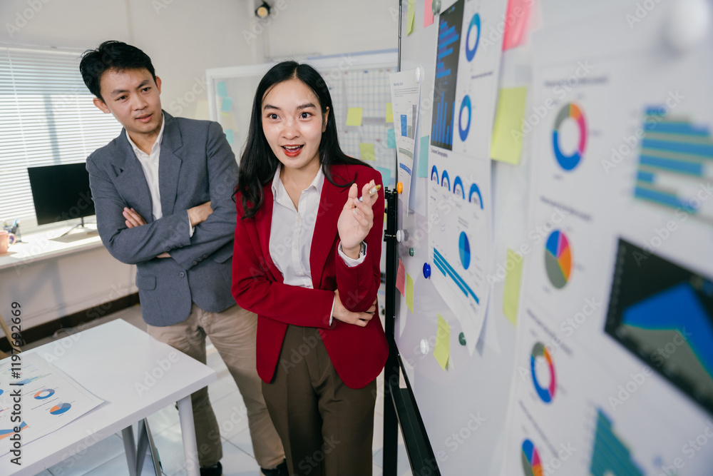 Poster businesswoman presenting charts and graphs on a whiteboard while engaging with a businessman in a mo