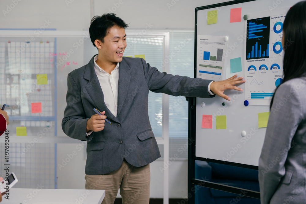 Poster young businessman explaining charts and statistics on whiteboard to his colleagues during an office 