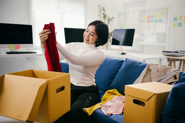 Young office worker is smiling while sorting through clothing items and placing them into donation boxes. She is participating in a charitable initiative