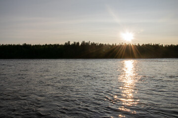 Sunset over forest and river with sunlight reflections on water. Etuväylä river glistening under sunset in Finland, Scandinavia. 