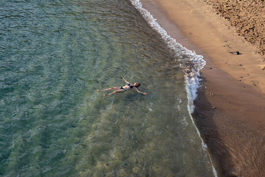 top view of woman floating in the sea near sandy beach
