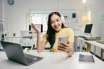 Young professional woman is using a smartphone and wearing headphones while participating in a business video call, gesturing with one hand as she engages in the conversation