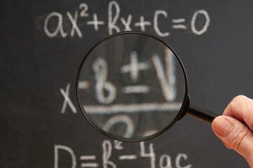Man with magnifying lens looks at a quadratic equation handwritten on a blackboard