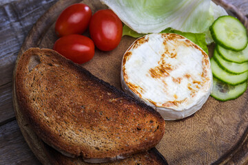 Grilled brie cheese with bread, cucumber, tomato and salad on wood plate. Vegetarian, healthy homemade food