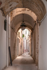 A narrow alleyway in Tunis adorned with historic architecture and a hanging lantern. The weathered walls and quiet atmosphere reflect the city's rich cultural heritage.