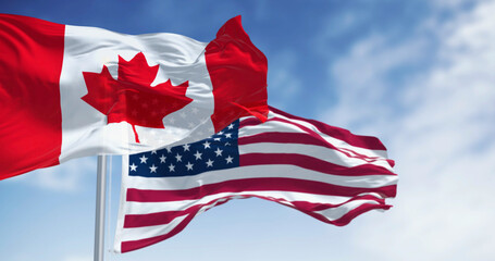 Canada and american national flags waving in the wind on a clear day