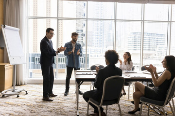Group of businesspeople applauding, finish formal meeting or corporate training event led by two young Arabian businessmen, team leaders or executives in modern skyscrapers building conference room