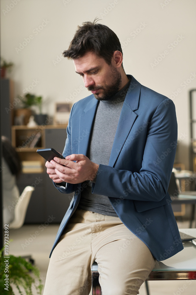 Aufkleber young serious male manager or broker in formalwear looking at screen of mobile phone while sitting o