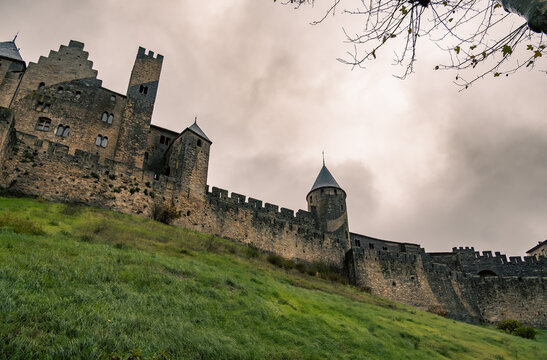 Medieval stone castle with towers of Carcassonne medieval fortress on a green grassy hill under a cloudy sky at twilight.