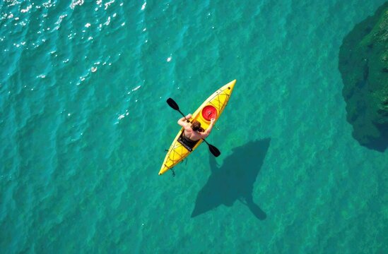 An overhead view of a man paddling a bright yellow kayak on clear azure water. Summer active holiday concept.