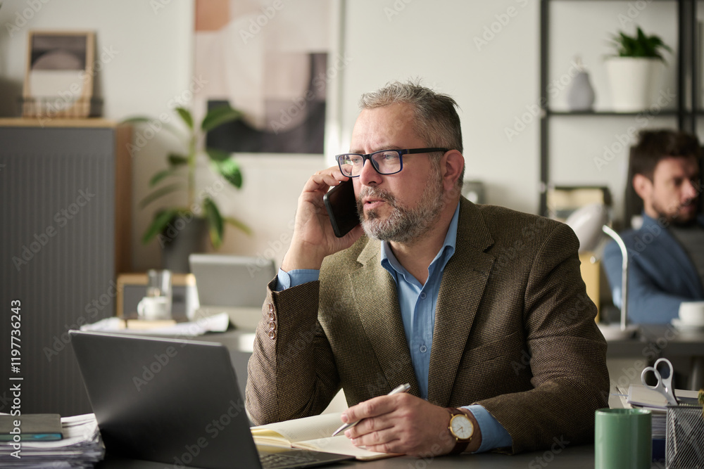 Poster Confident male director of firm with smartphone by ear organizing work in front of laptop and making notes in notebook