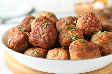 Tasty cooked meatballs with green onion in bowl on white table, closeup