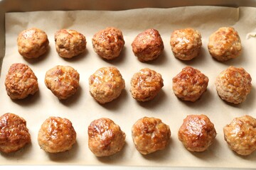 Many delicious meatballs on parchment in baking dish, above view