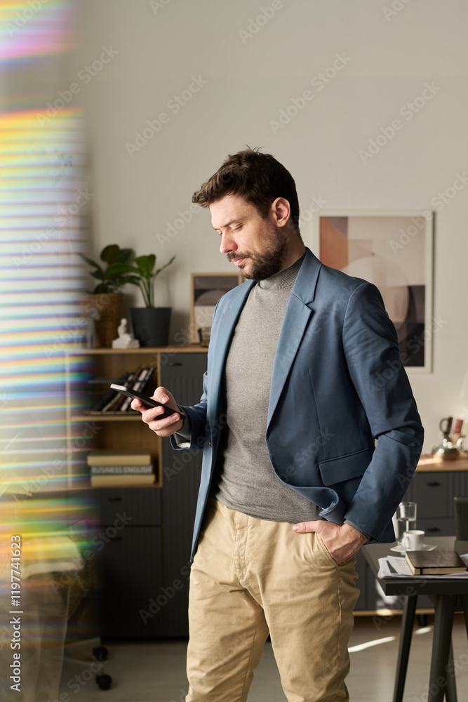 Aufkleber young serious manager looking through message on screen of mobile phone and texting while standing b