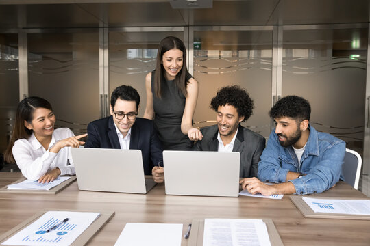 Creative business team gathered in office boardroom working together on joint online project, develop presentation using laptop, share startup ideas or design project, discuss insights, brainstorming