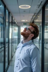 Fototapeta premium Man with beard and glasses looking at computer screen, reflective office environment.