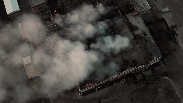 Aerial top view of city block on fire with thick smoke rising, damaged rooftops and urgent rescue situation from drone vantage, urban disaster.