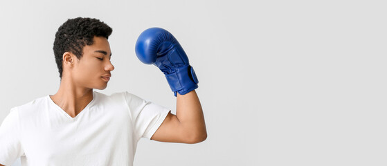 Young African-American man with boxing glove on light background. Immunity concept