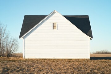 Obraz premium White farmhouse stands against a clear blue sky in rural landscape at dawn, showcasing simple architecture and tranquil surroundings