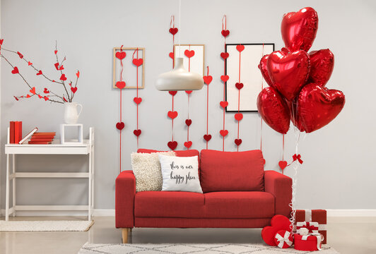Interior of living room decorated for Valentine's Day with balloons, sofa and gifts